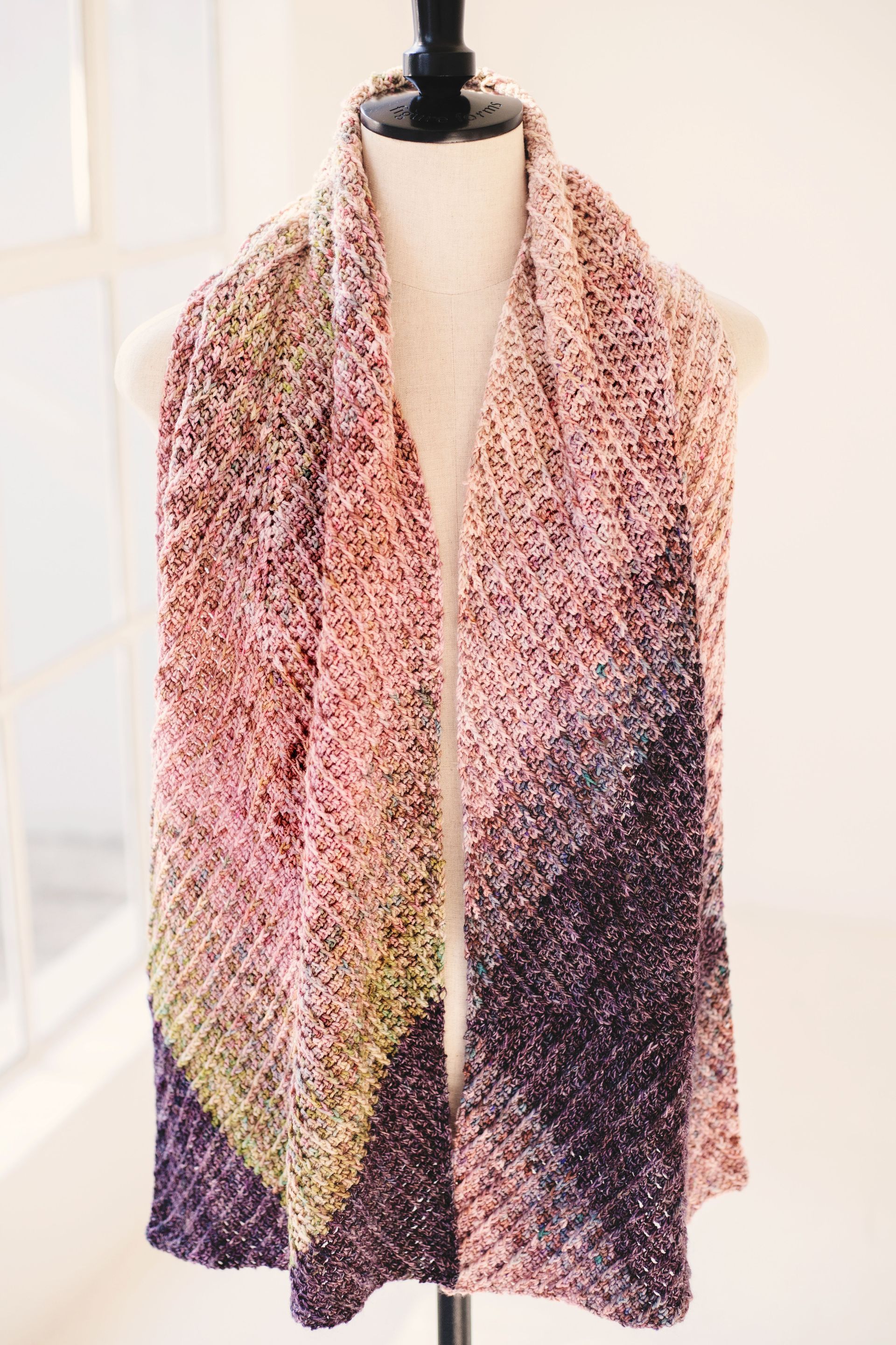 Pink and purple ombre scarf draped on a mannequin in front of a window.