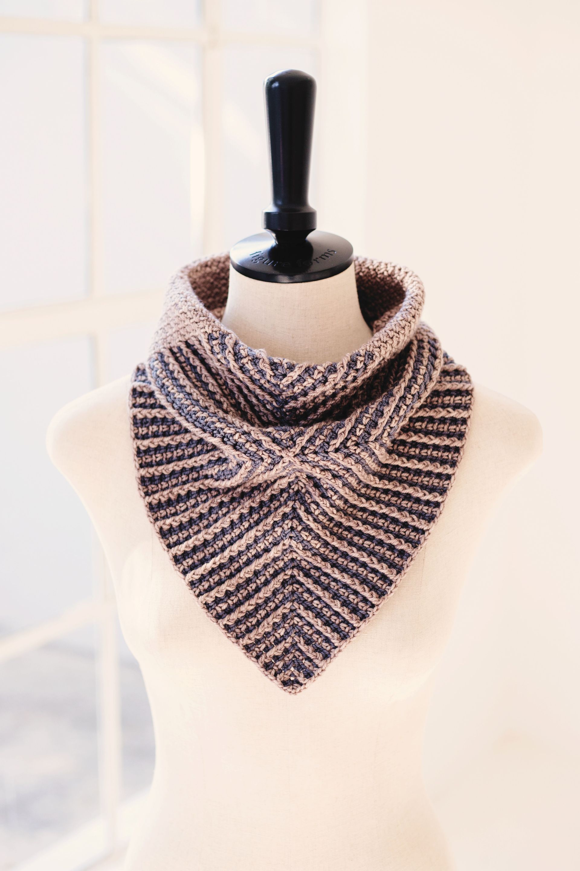 Knitted cowl scarf on a mannequin, two-toned brown and black, triangular shape with a folded collar.