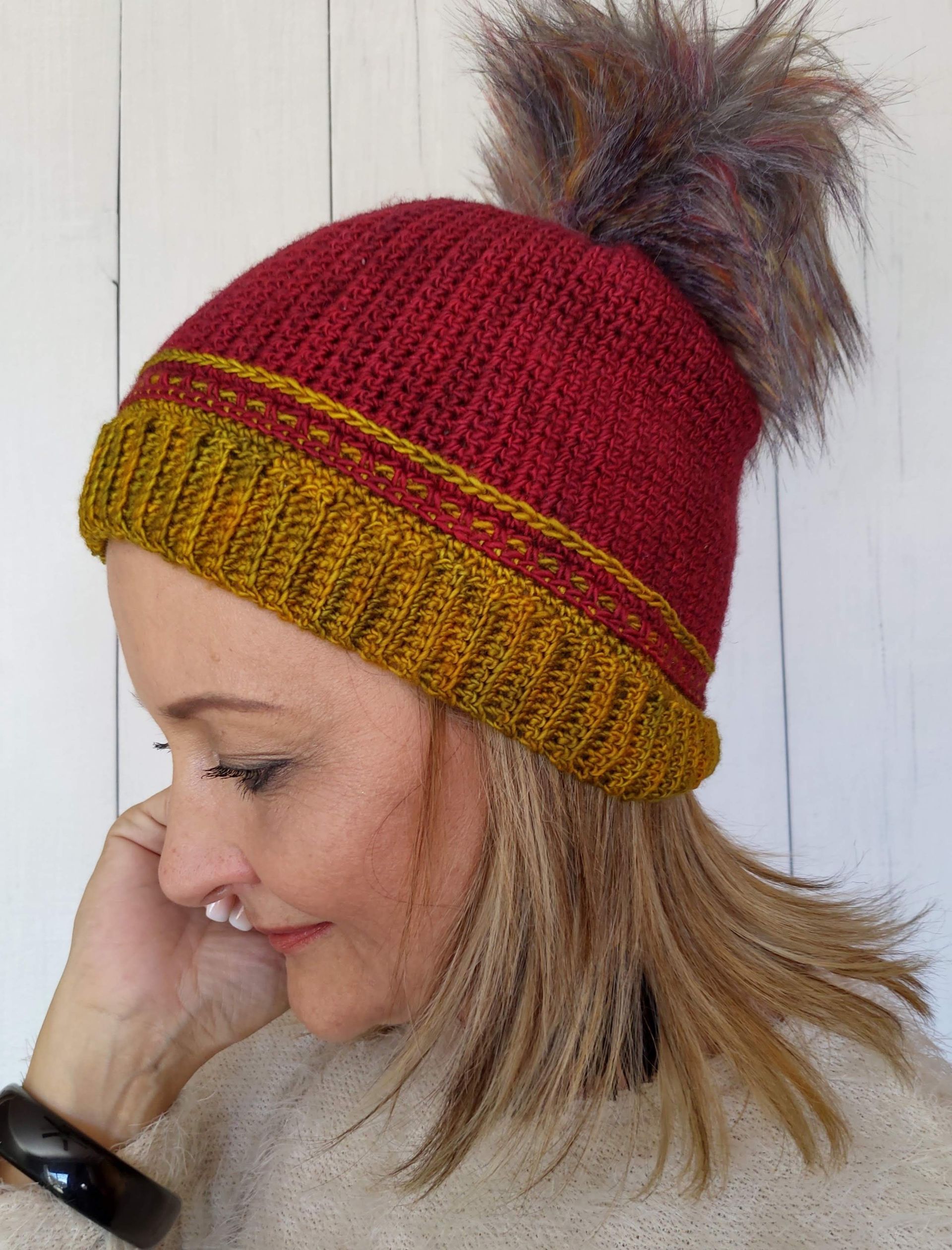 Woman wearing a red and gold knitted hat with a fur pom-pom.