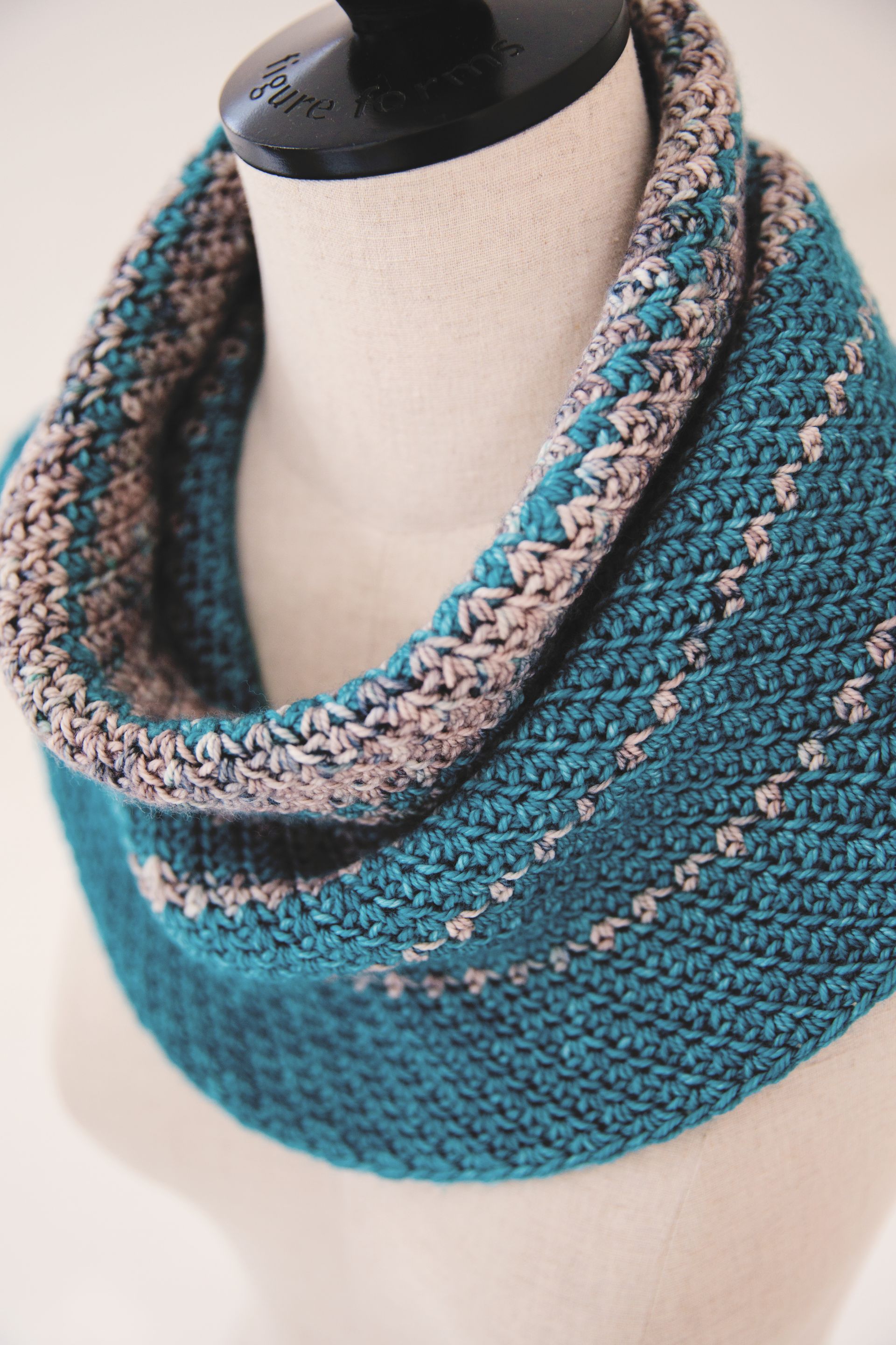 Teal and tan knitted cowl on a mannequin, with textured stitch and stripes.