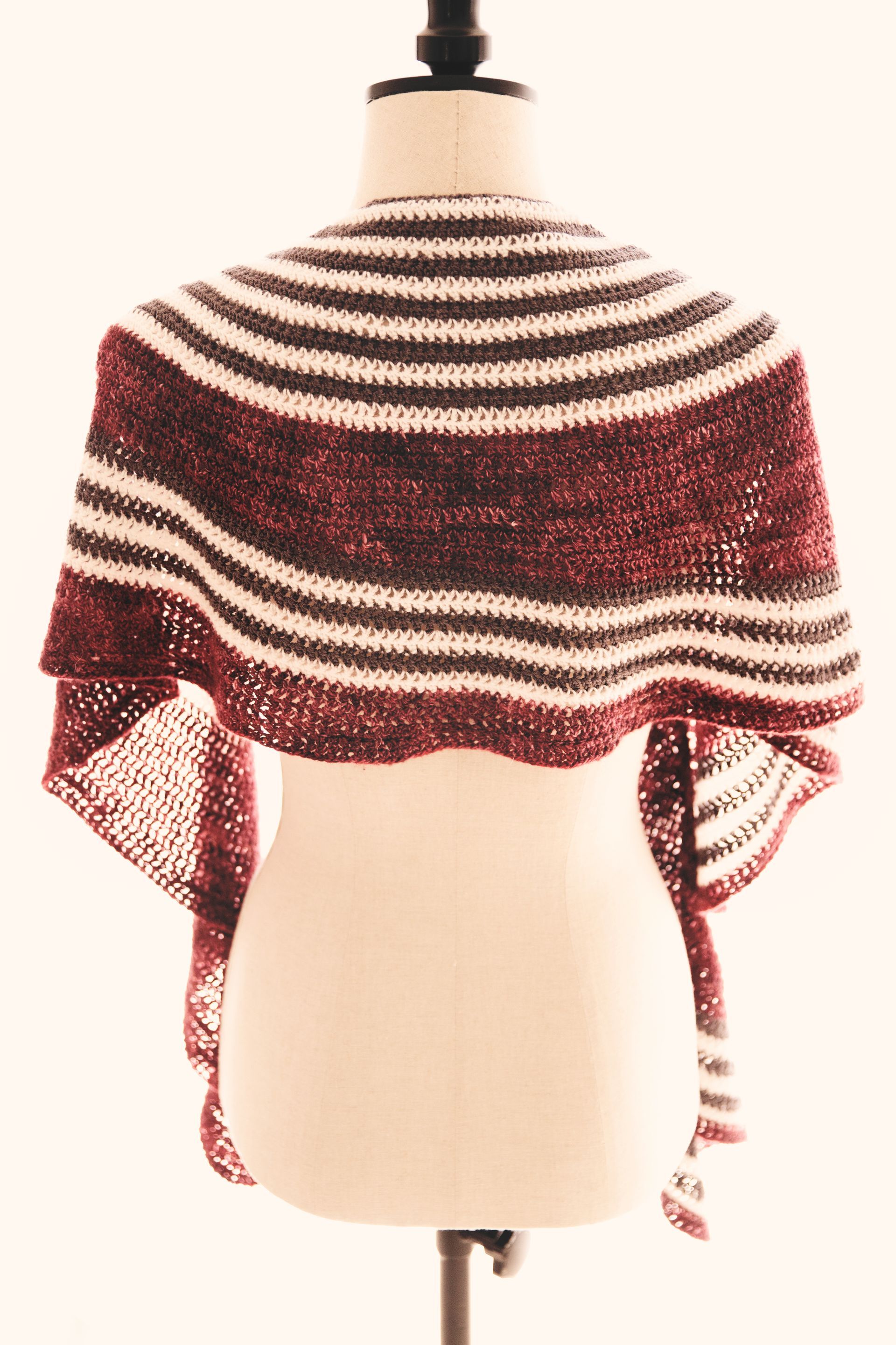 Crocheted shawl on a mannequin. Burgundy, brown, and white horizontal stripes.