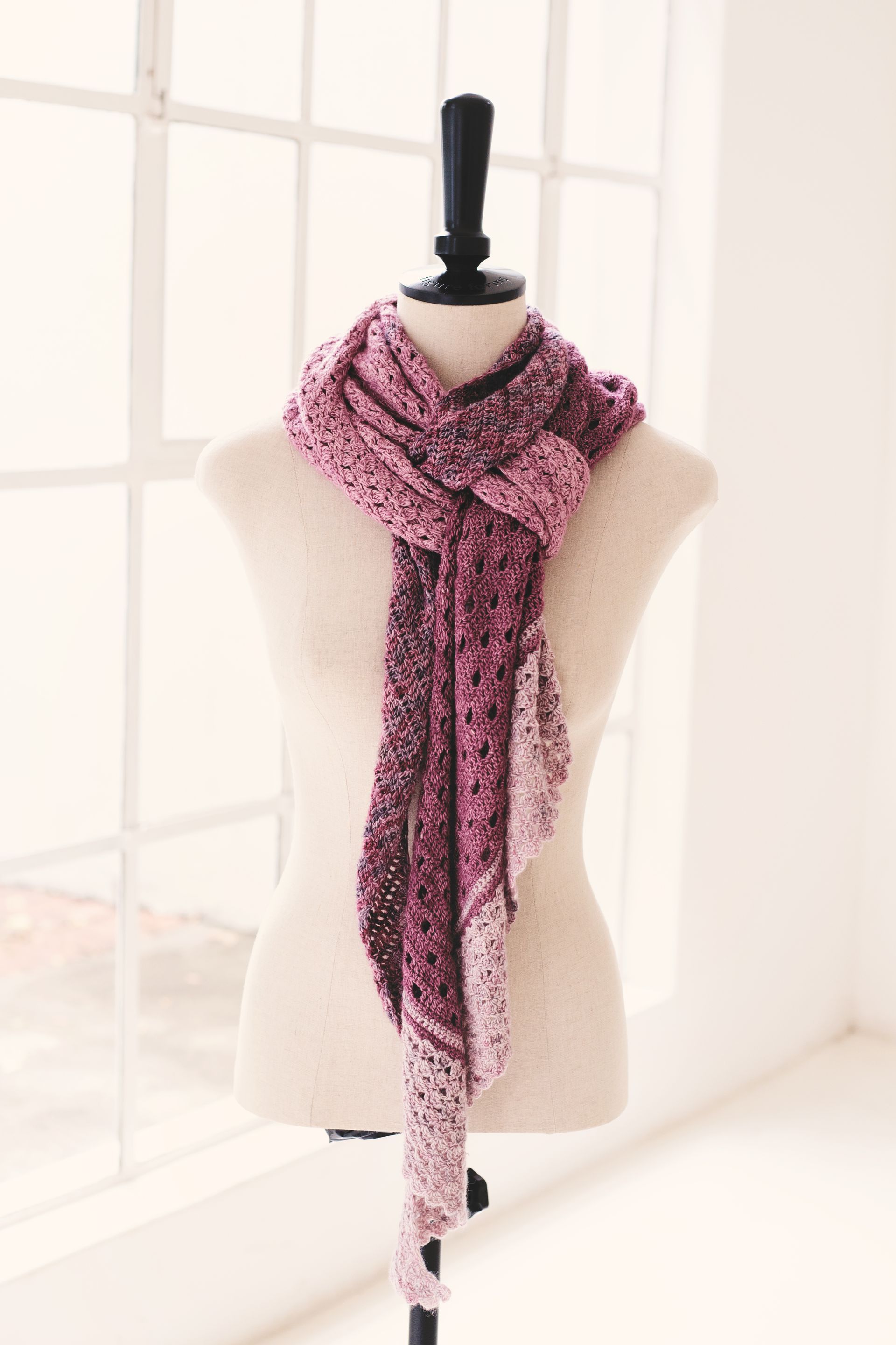 Pink and purple crocheted scarf draped on a mannequin in front of a window.