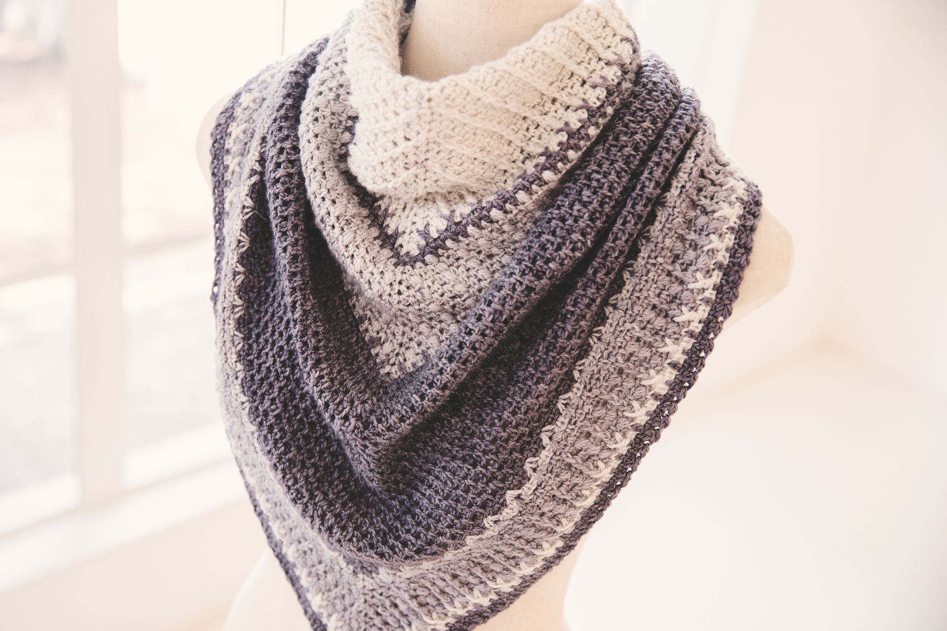 Triangular crocheted shawl in shades of blue, gray, and white displayed on a mannequin.