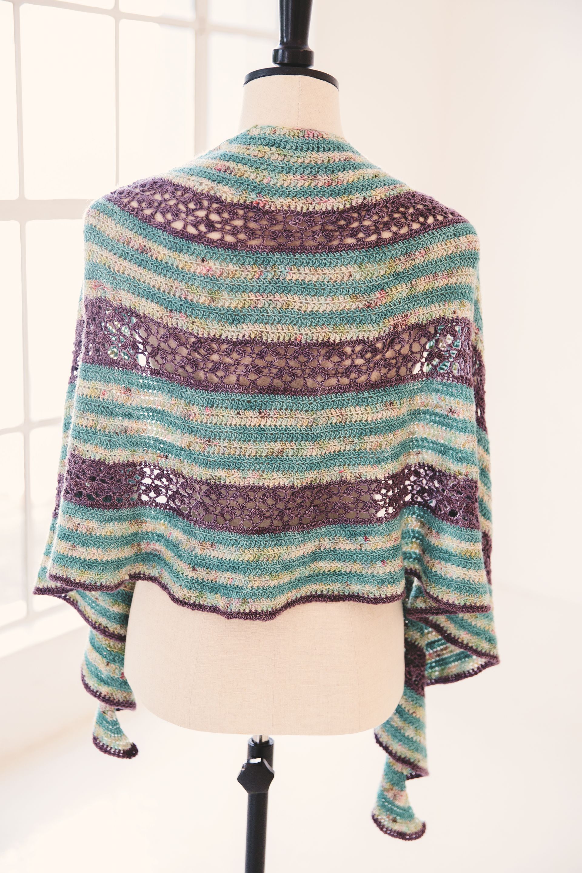 Crocheted shawl on a mannequin, featuring teal, purple, and beige stripes.