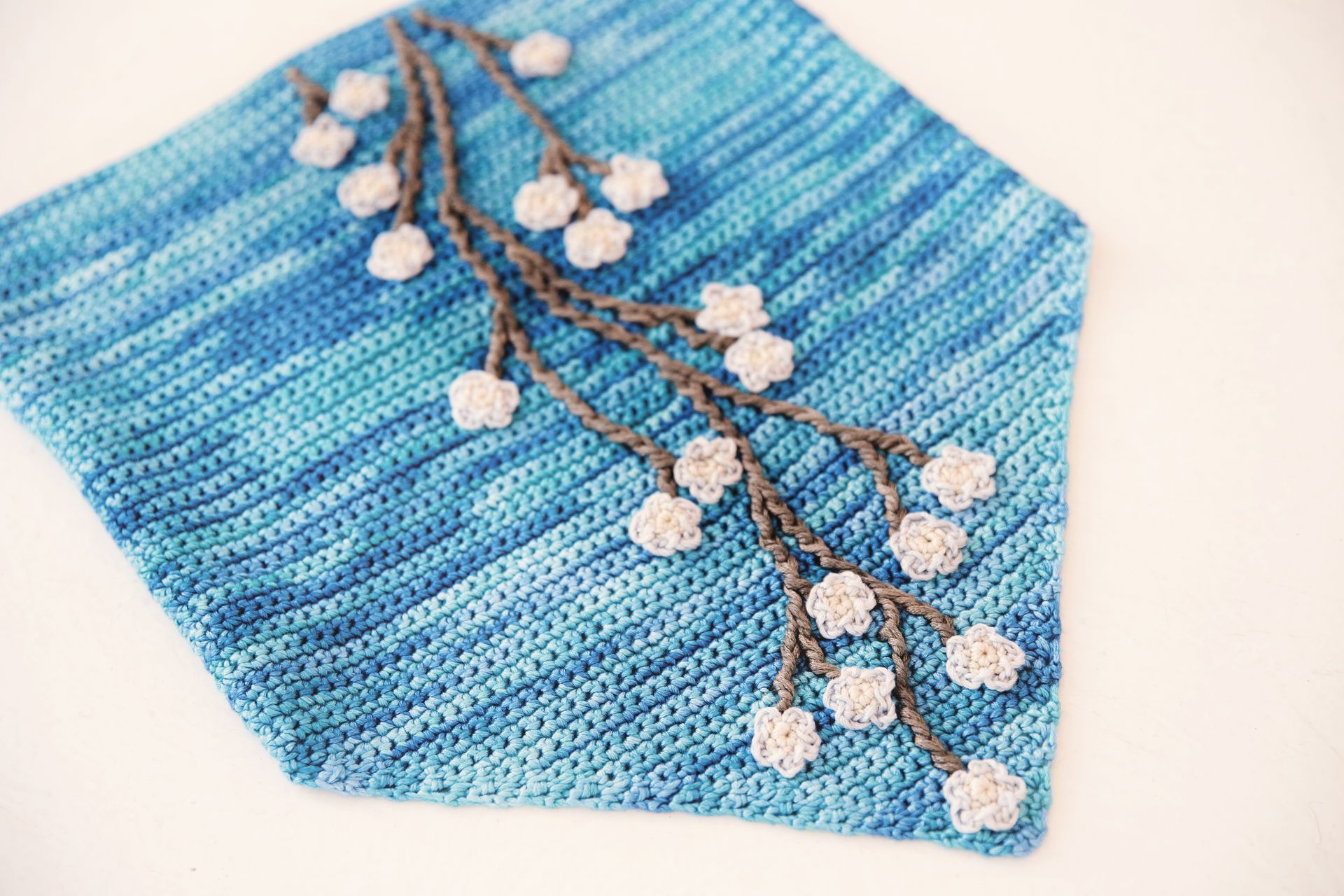 Crocheted blue scarf with grey floral vine and white flowers.