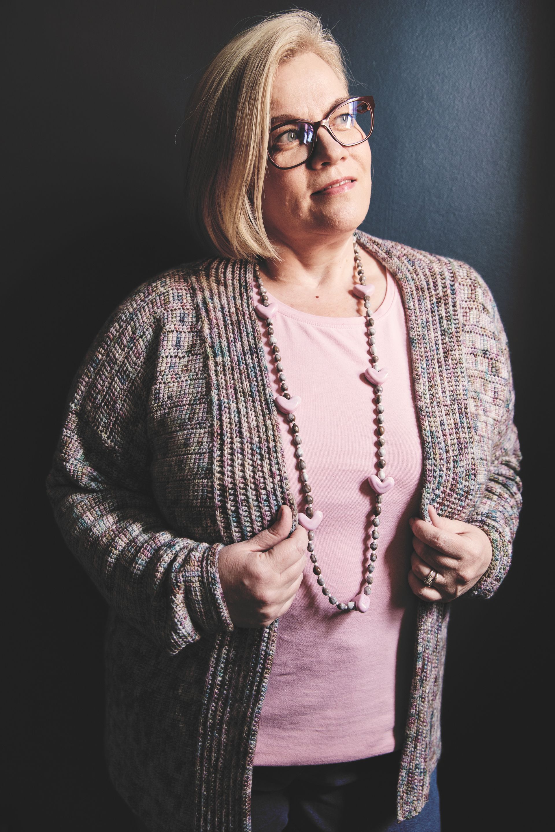 Woman with blonde hair wearing glasses and a patterned sweater, looking upwards, smiling.