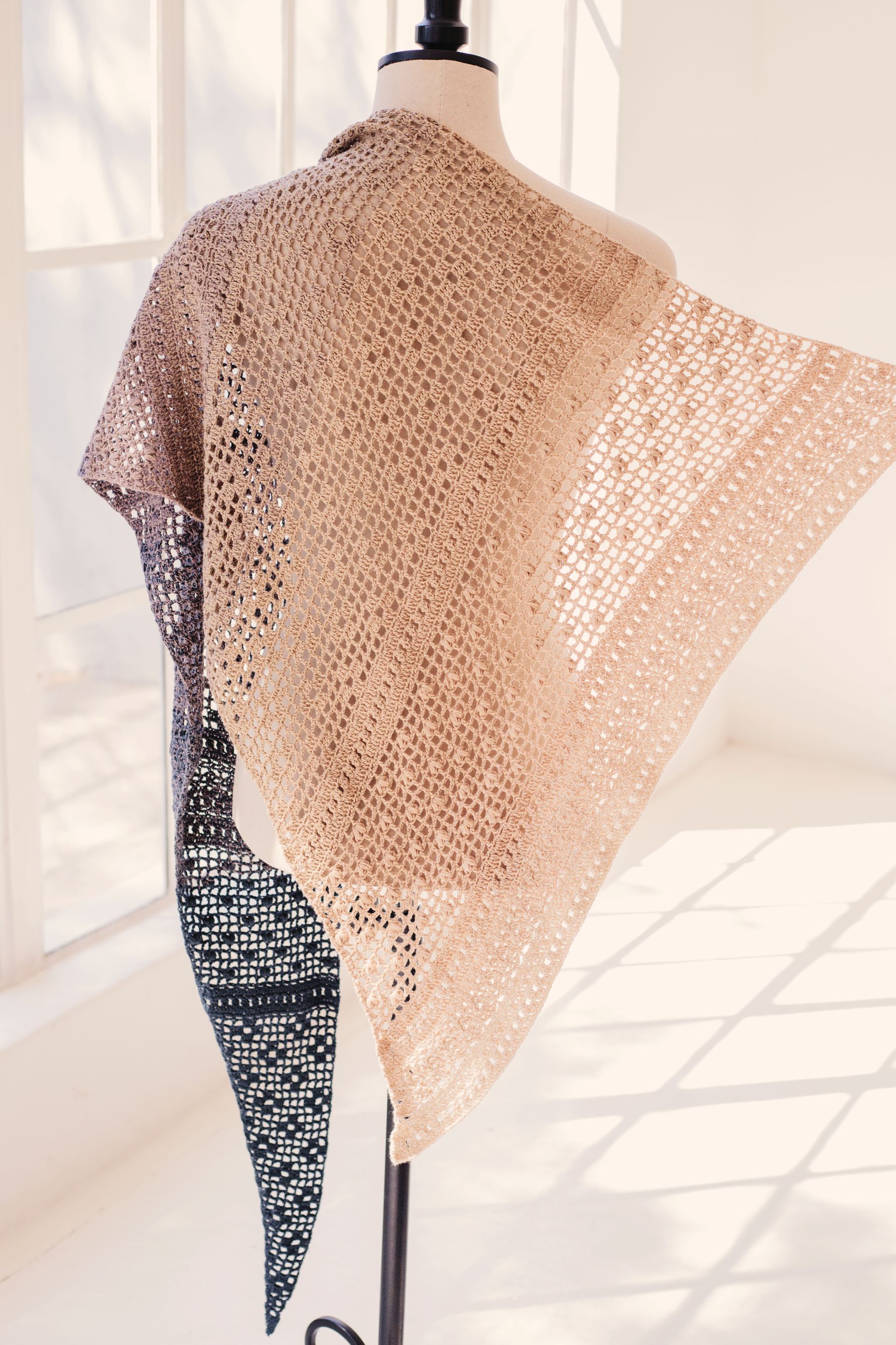 Light brown and tan crocheted shawl draped over a mannequin against a window.
