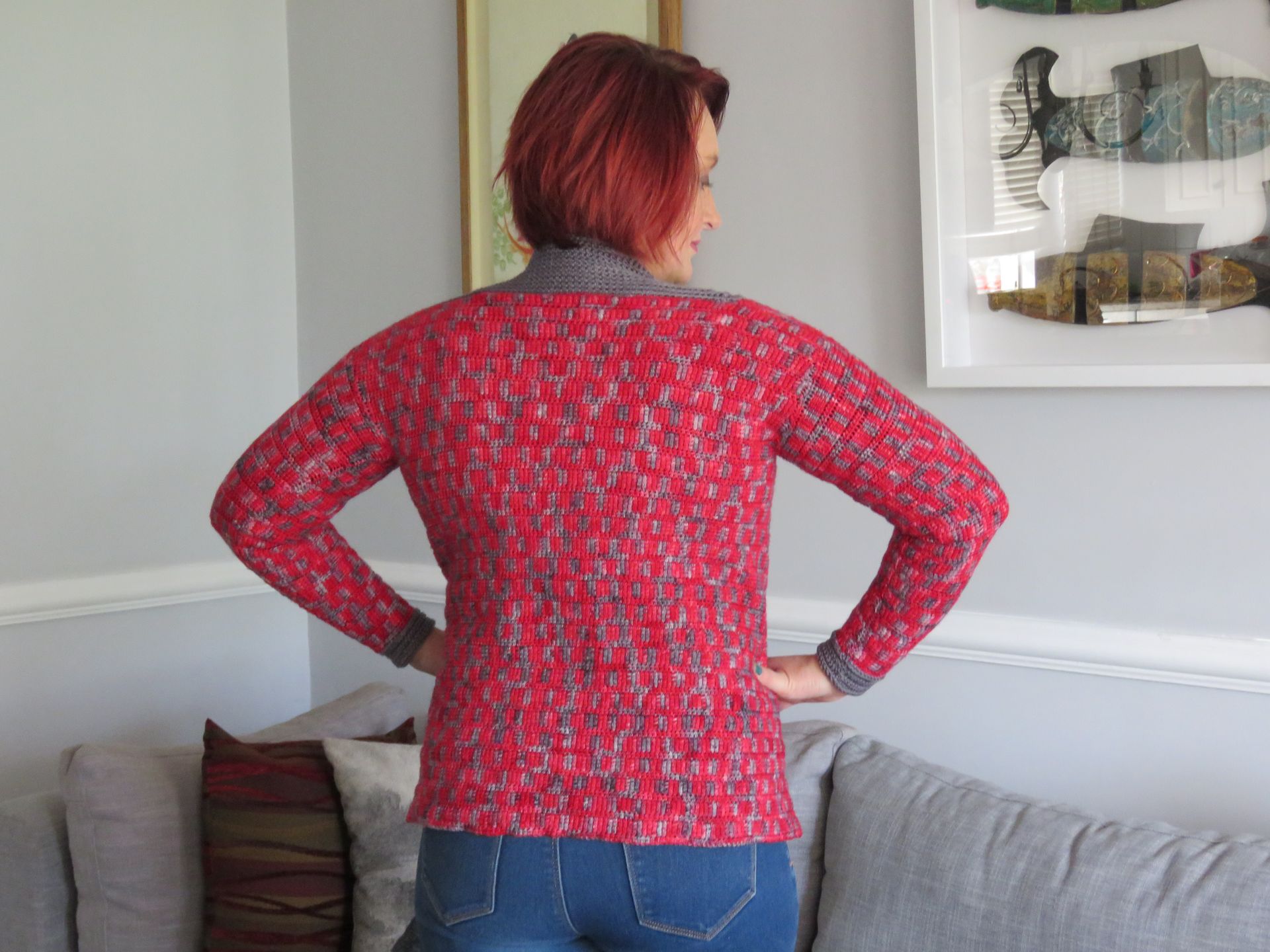 Woman in red patterned sweater with grey trim, hands on hips, facing away.