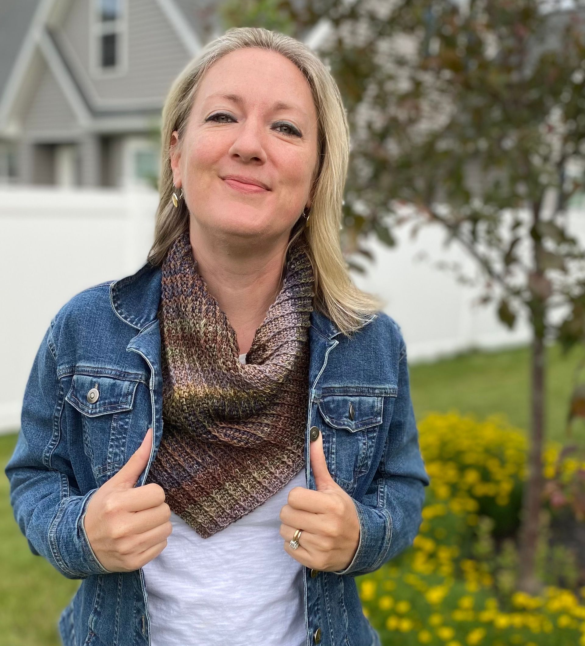 Woman in denim jacket with a colorful knitted scarf, smiling outside.