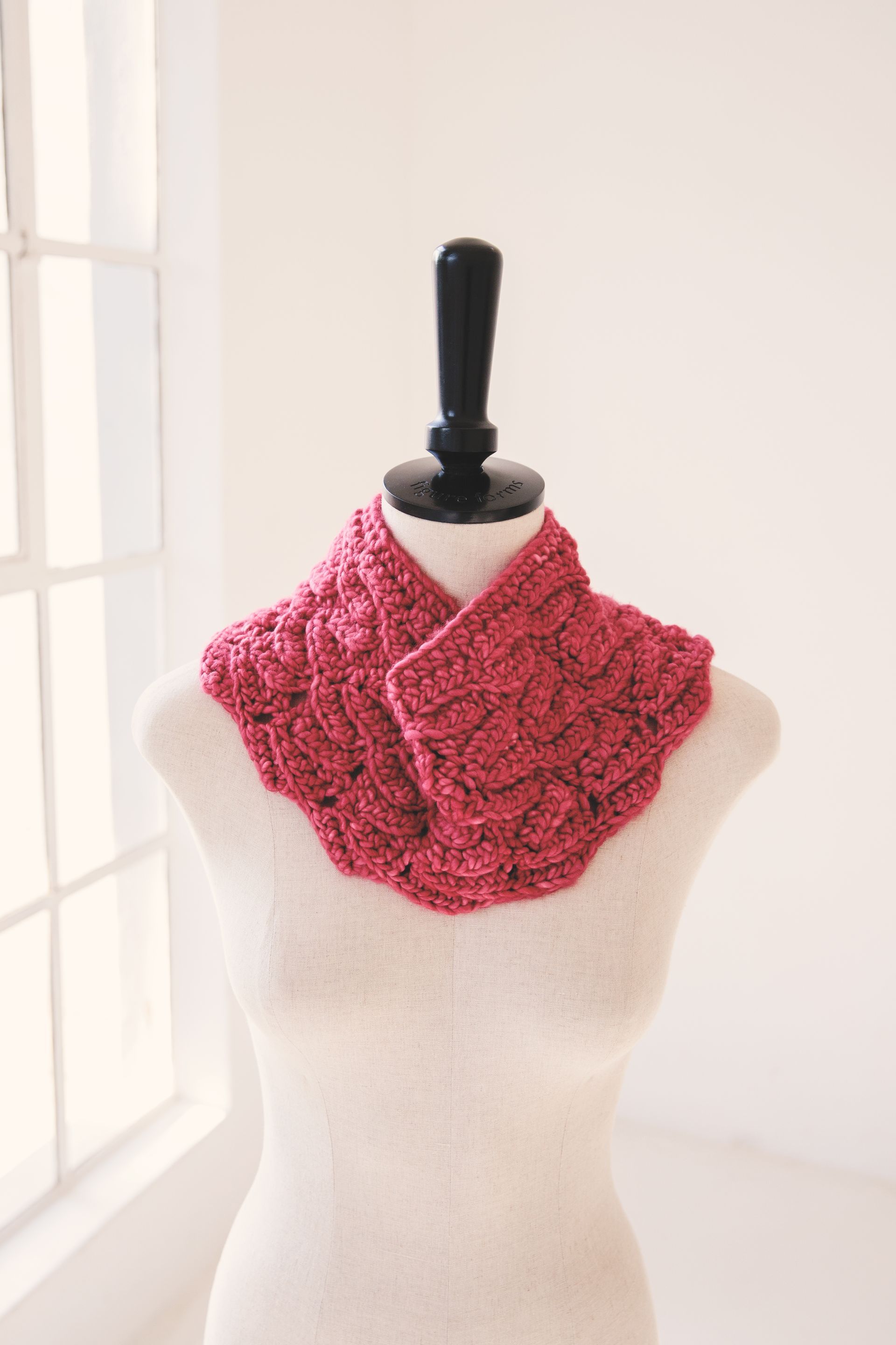 Pink crocheted cowl on a mannequin, displayed in front of a window.