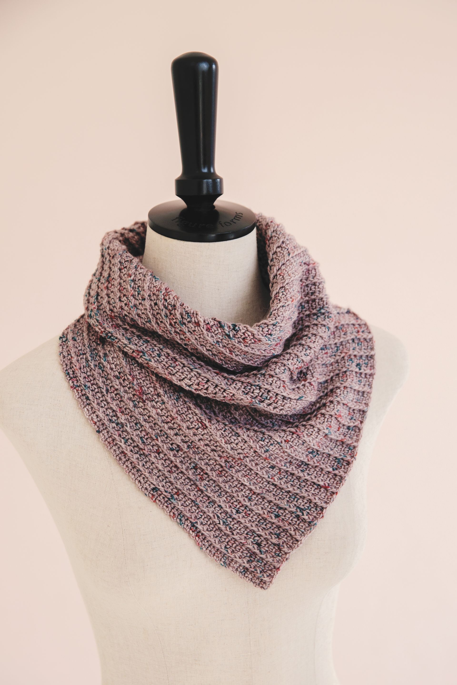 Pink and purple knit cowl on a mannequin with a black stand against a light pink background.