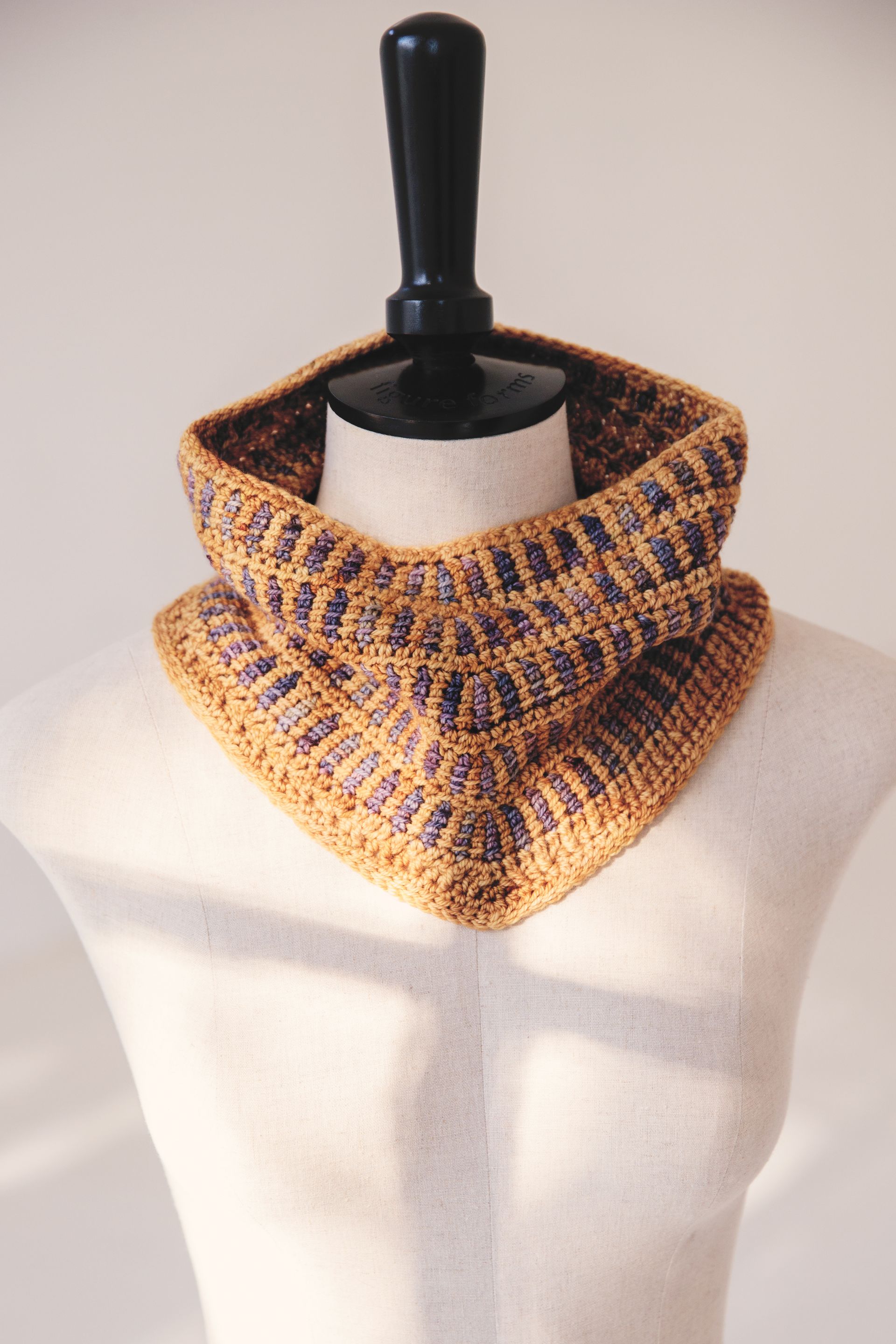 Crocheted cowl in mustard yellow and brown tones, displayed on a mannequin.