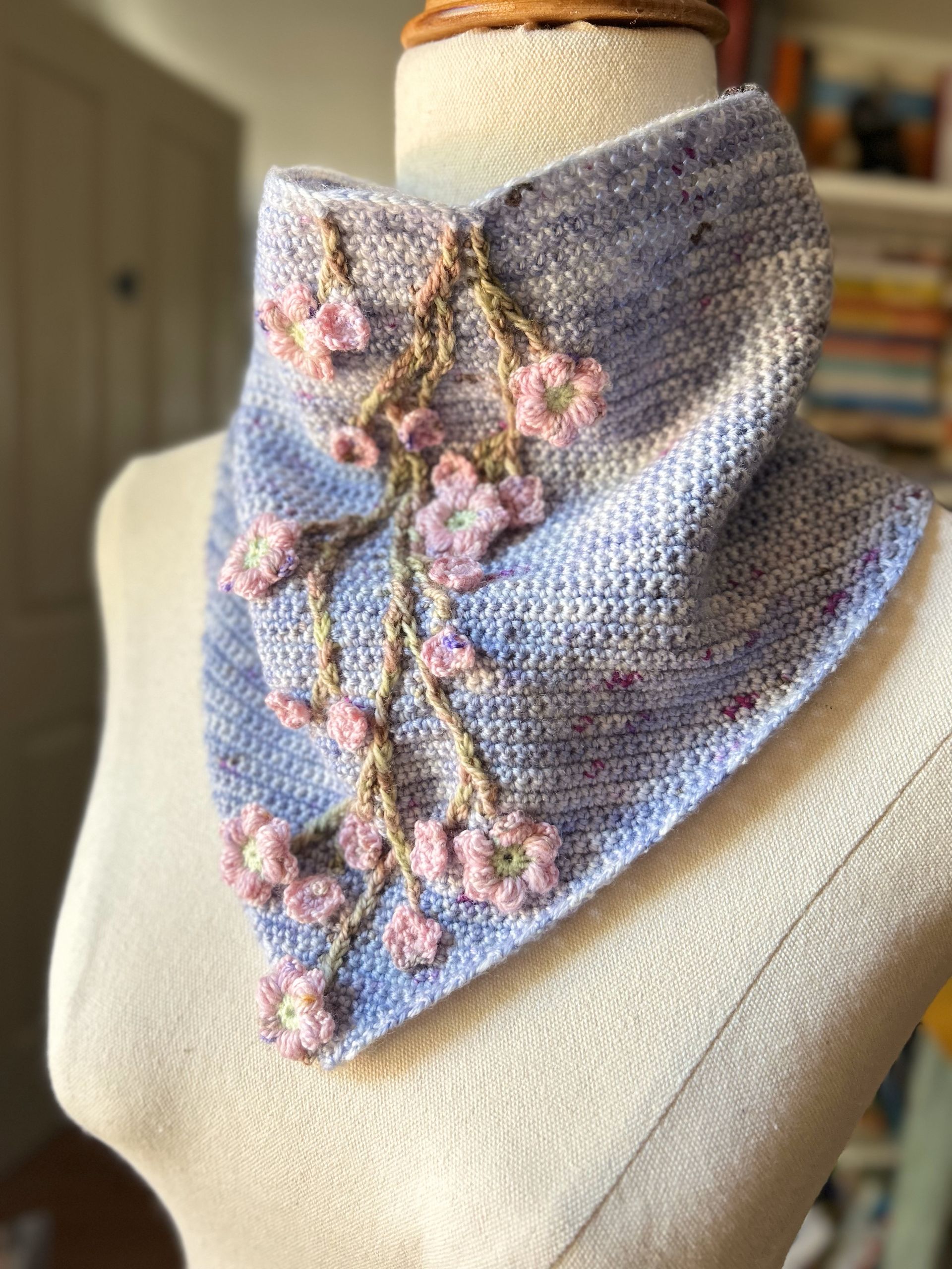 Blue and purple knit cowl on a mannequin, adorned with pink and tan floral embellishments.