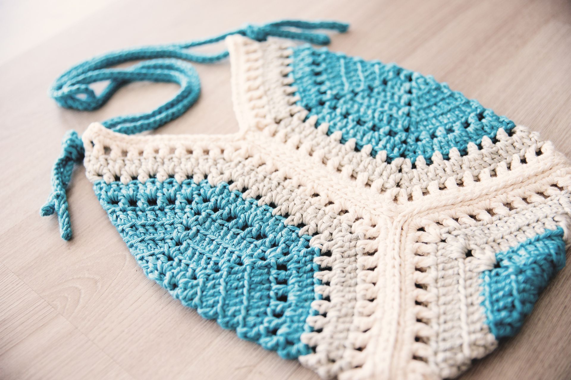 Crocheted shoulder bag in teal and cream with a blue strap.