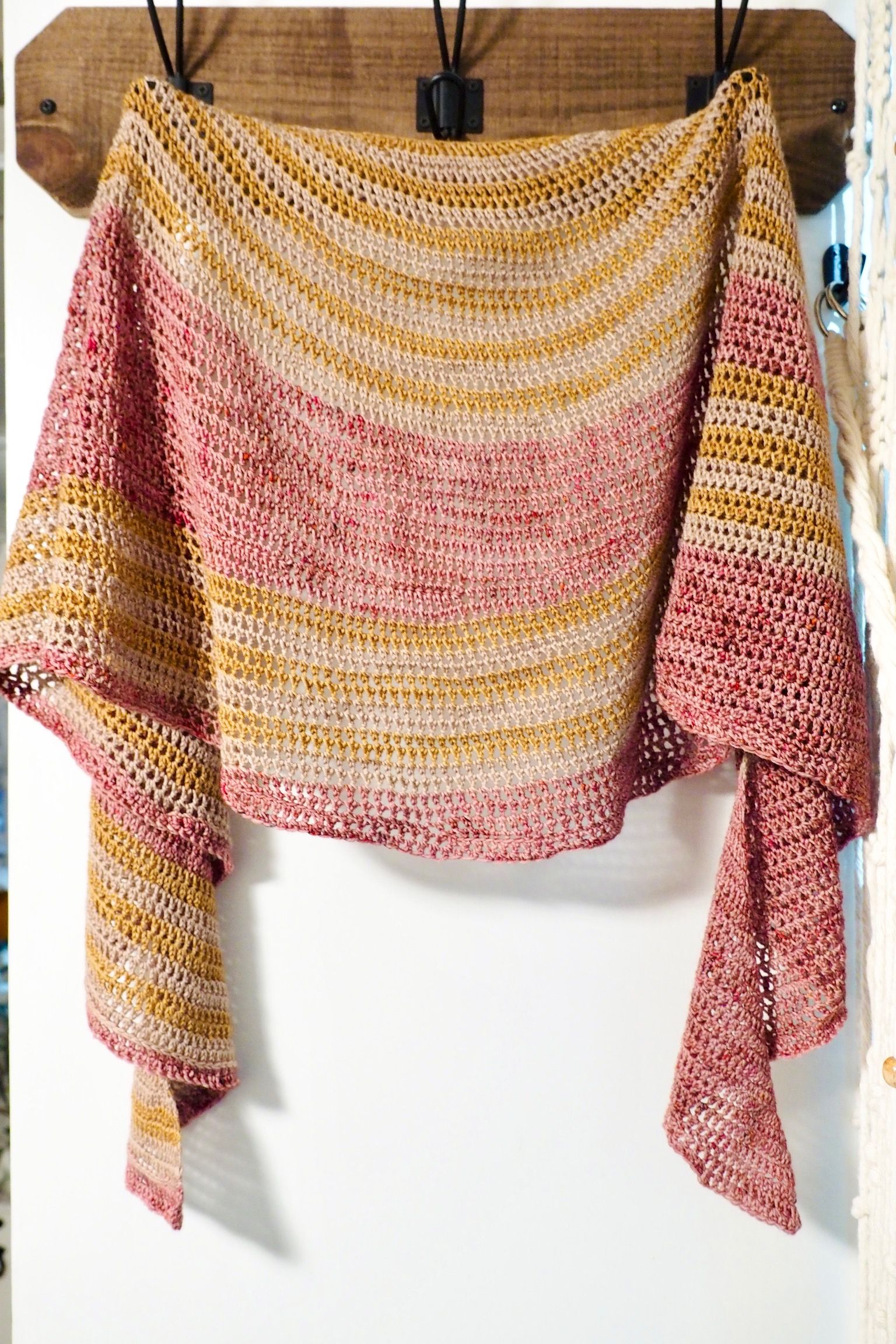 Pink and gold crocheted shawl hanging on a wooden rack.