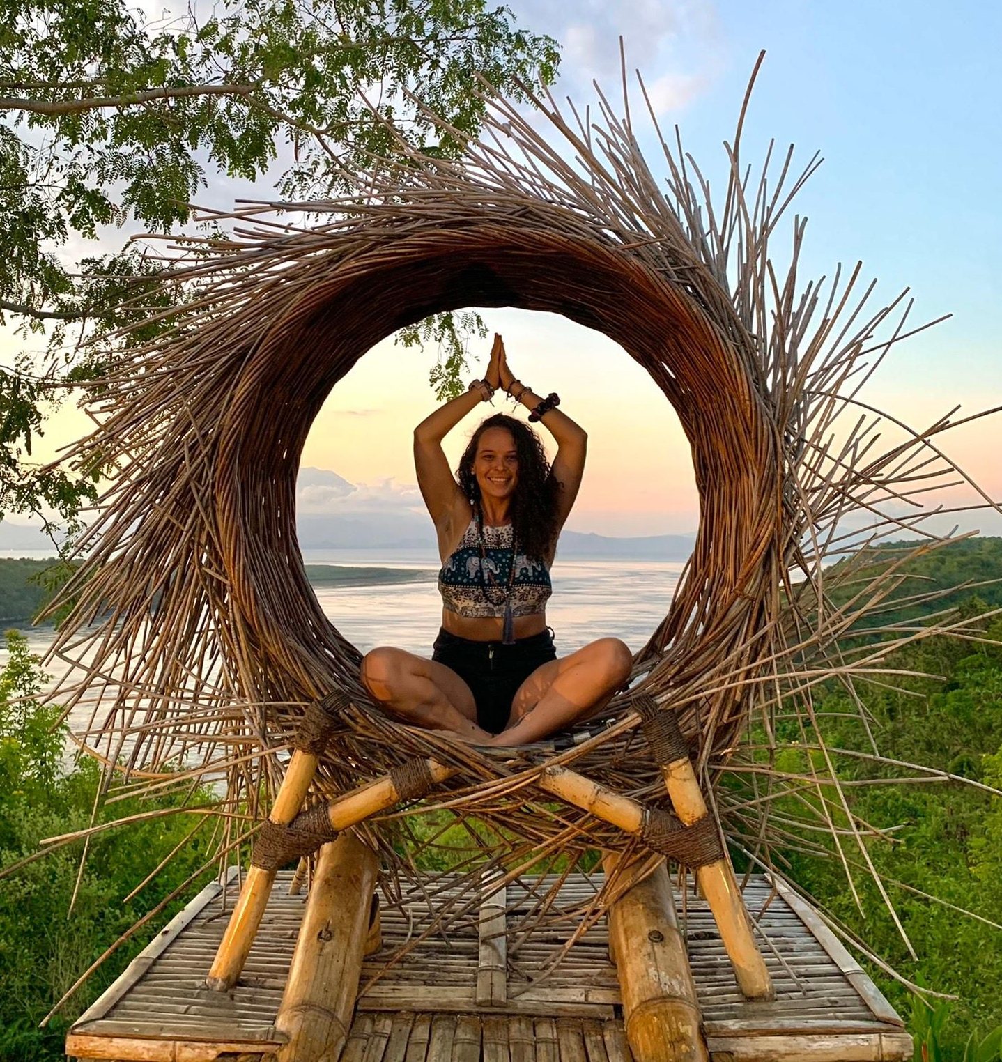 Woman in light blue crop top and beige pants poses outdoors in front of trees.