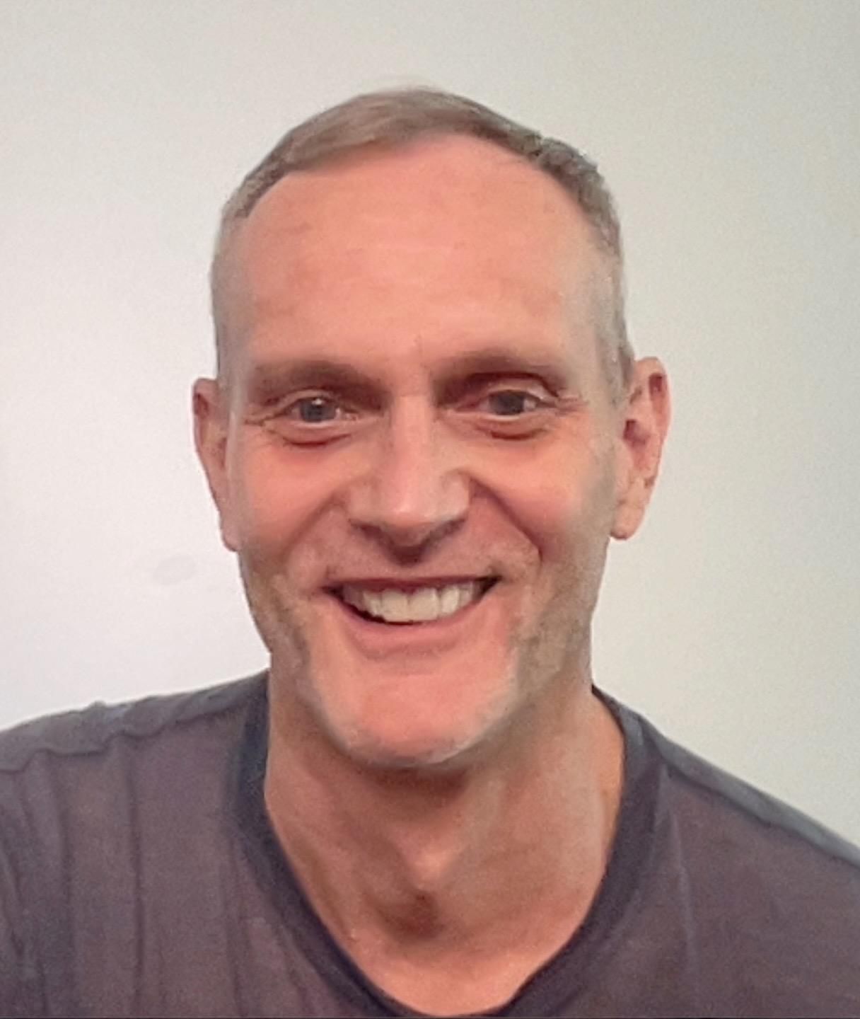 A smiling person sits on a boat bench, wearing a patterned summer dress, with waterfront houses in the background.