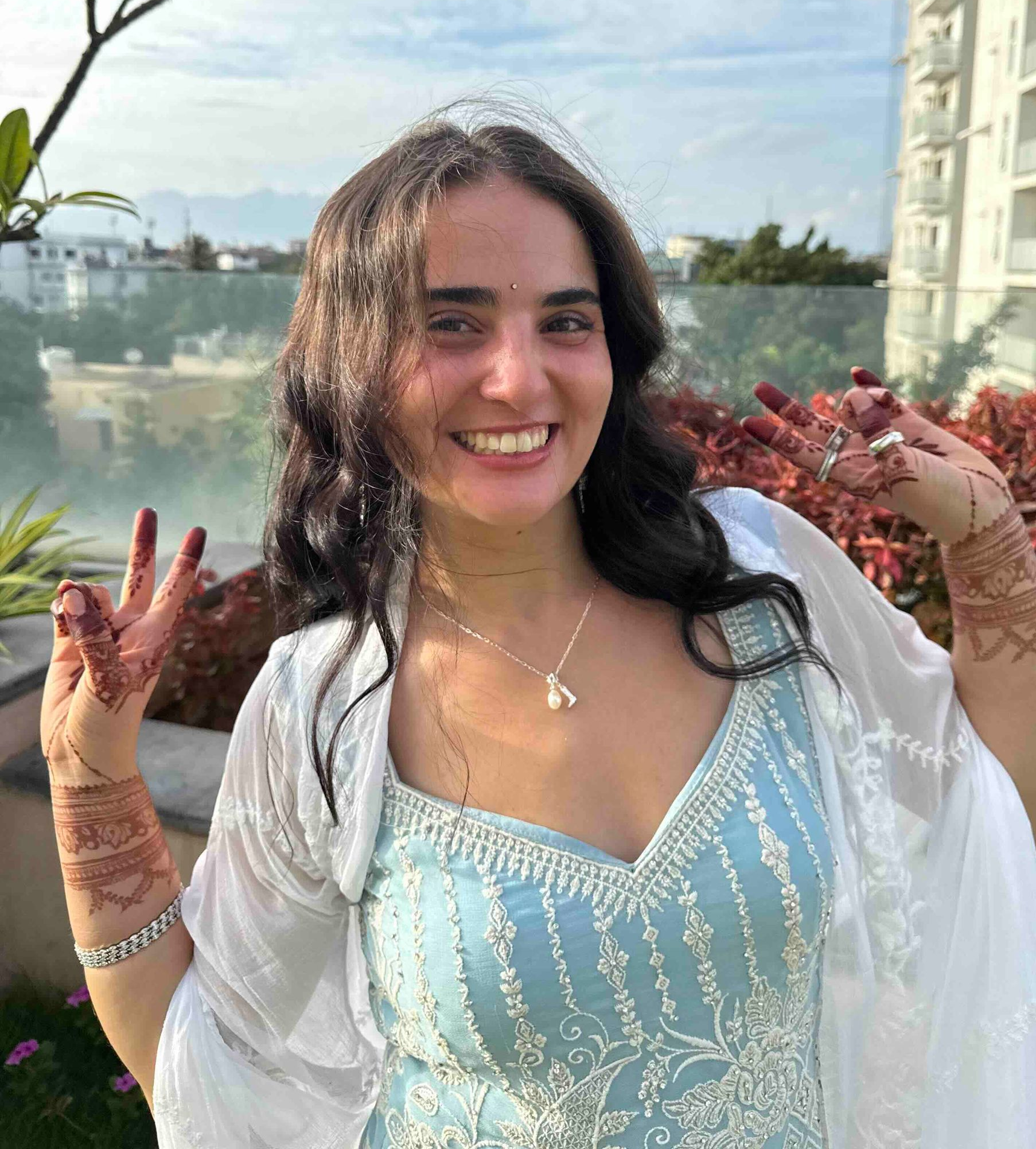 Woman in light blue crop top and beige pants poses outdoors in front of trees.