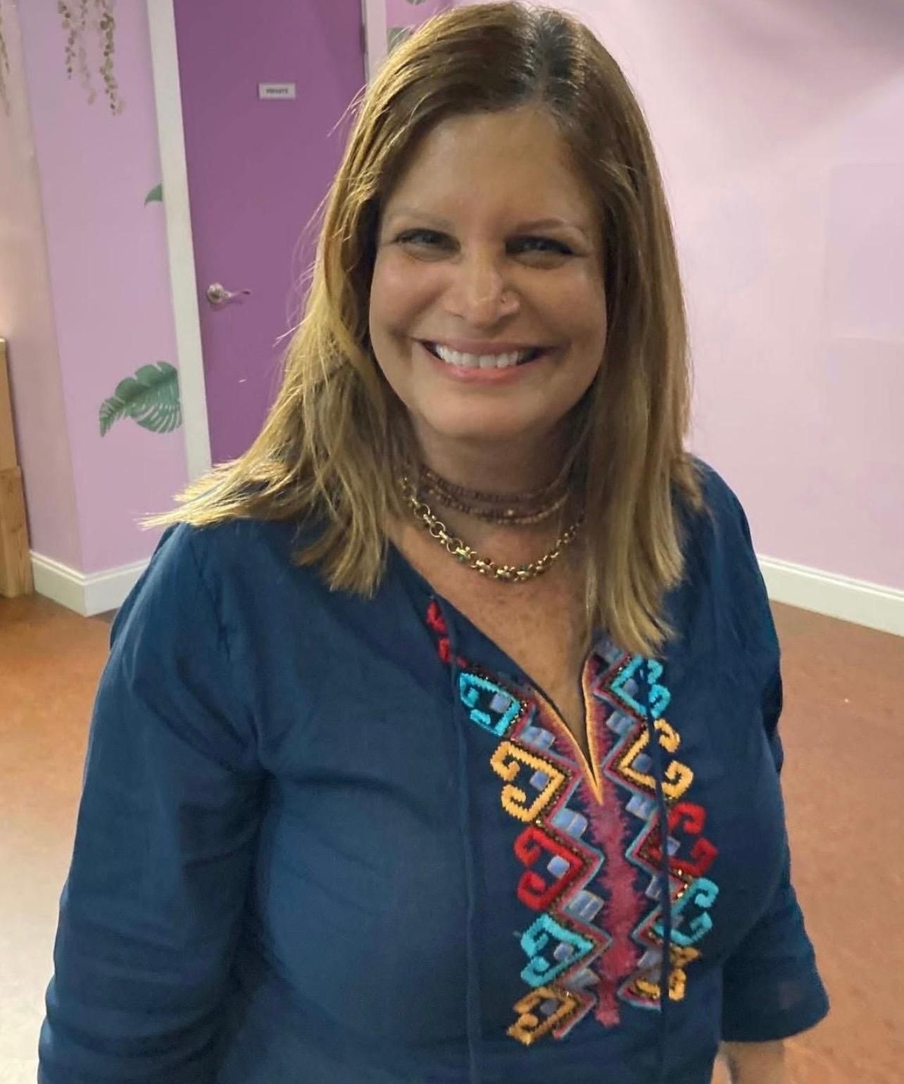 Woman in light blue crop top and beige pants poses outdoors in front of trees.