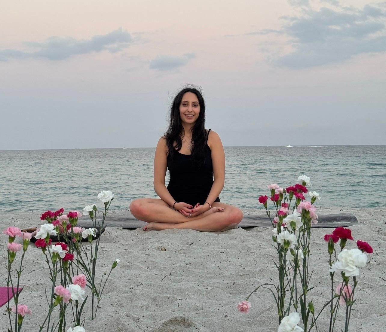 Woman in light blue crop top and beige pants poses outdoors in front of trees.