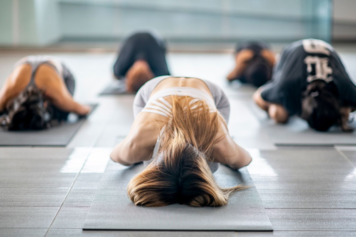 People in yoga class, resting in child's pose, on mats.