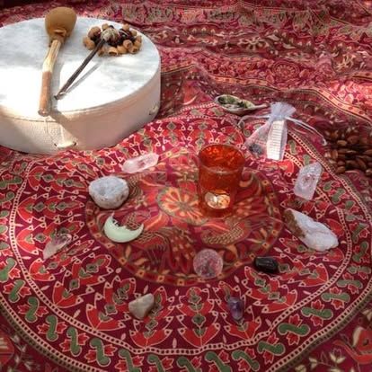 A spiritual altar with drum, crystals, candle, and other ritual items on a patterned red cloth.