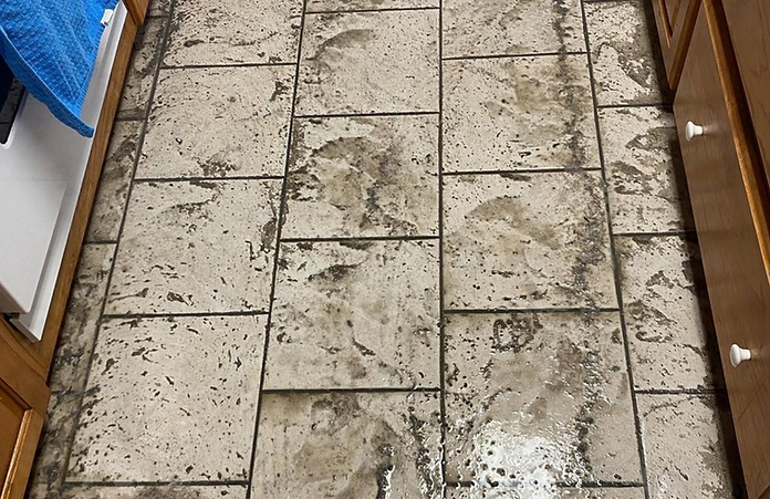 A kitchen floor with dirty tiles and wooden cabinets.