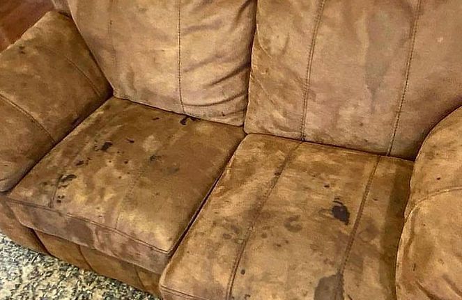 A brown leather couch with stains on it is sitting on a rug.