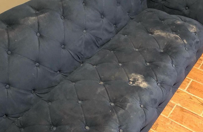 A dirty black couch is sitting on a tiled floor.