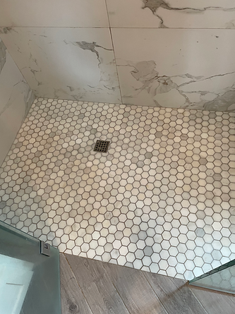 A shower stall with a honeycomb tile floor and a drain.