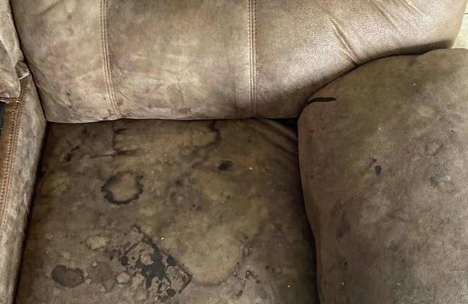 A close up of a dirty leather chair with stains on it.