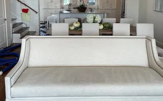 A white couch in a living room with a dining table in the background