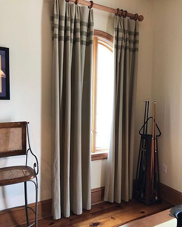 A living room with a chair , curtains , and a pool cue.