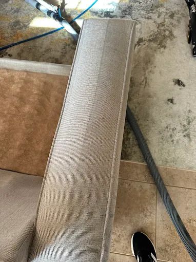 Cleaning a light-colored sofa; one side is clean, the other is dirty, on a tiled floor.