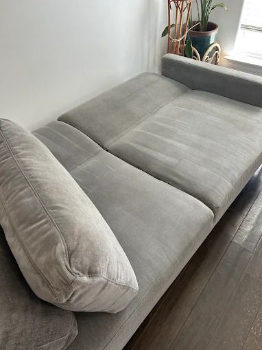 Gray sectional sofa with a large pillow against a white wall and hardwood floor.