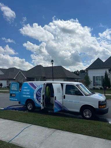A white service van parked on a residential street with open doors. Blue hose extends to a house. Cloudy sky.