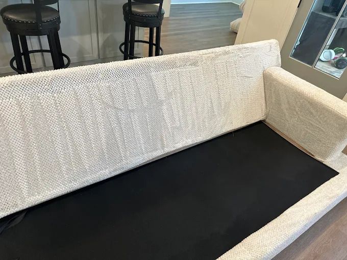 Cream-colored couch with a black cushion, showing the back and right arm. Two black bar stools are in the background.