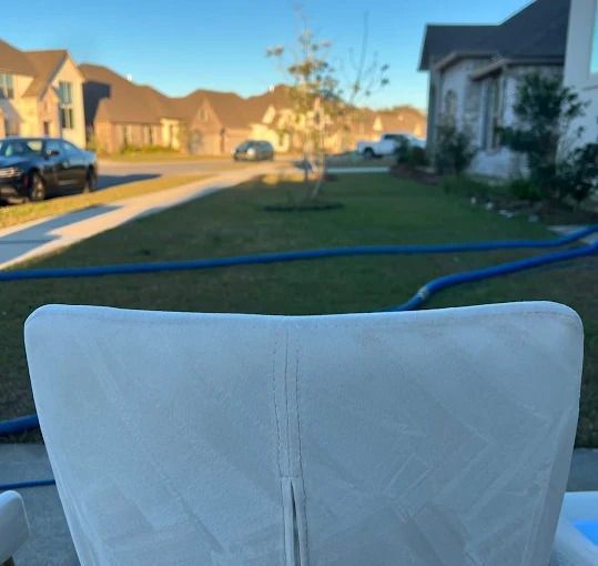 Back of a white chair on a patio, with a suburban street and houses in the background.