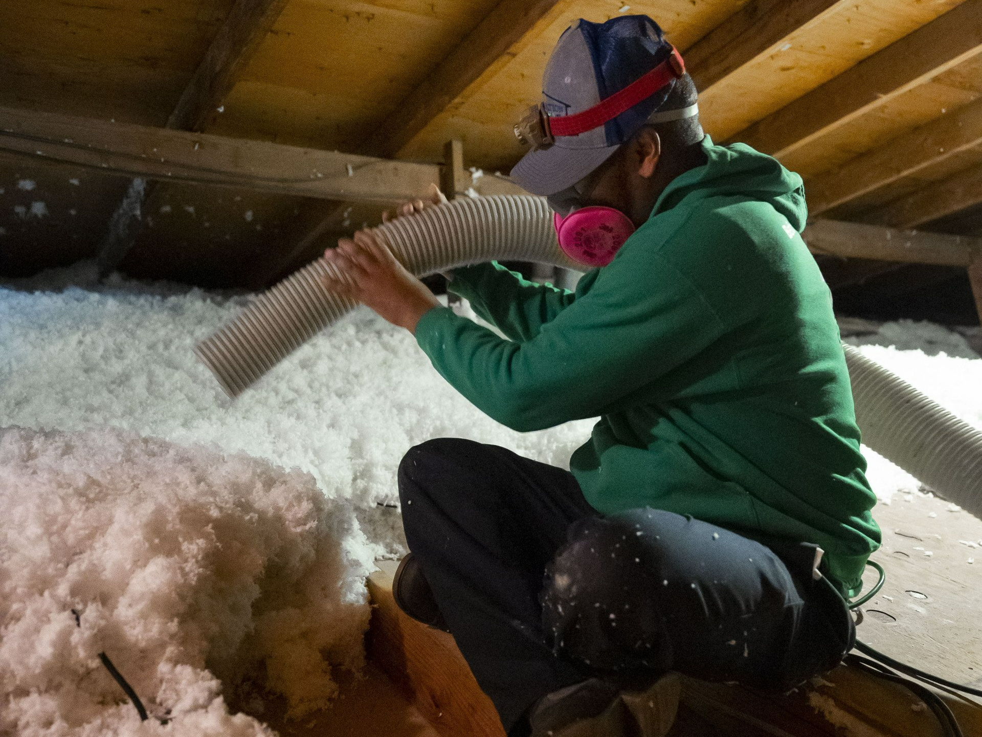 A man in a green hoodie is blowing insulation into an attic.
