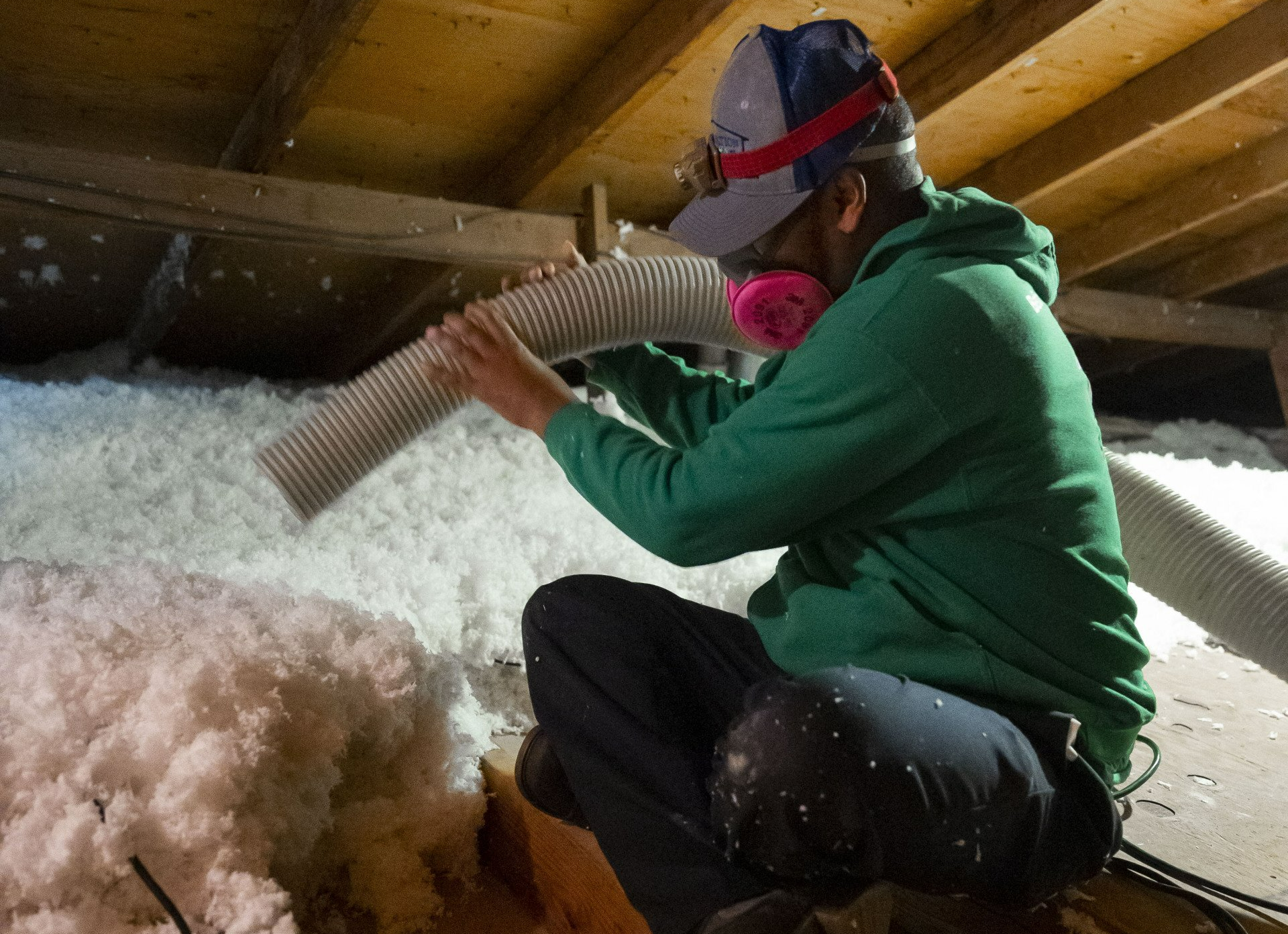 A man wearing a mask is blowing insulation into an attic.