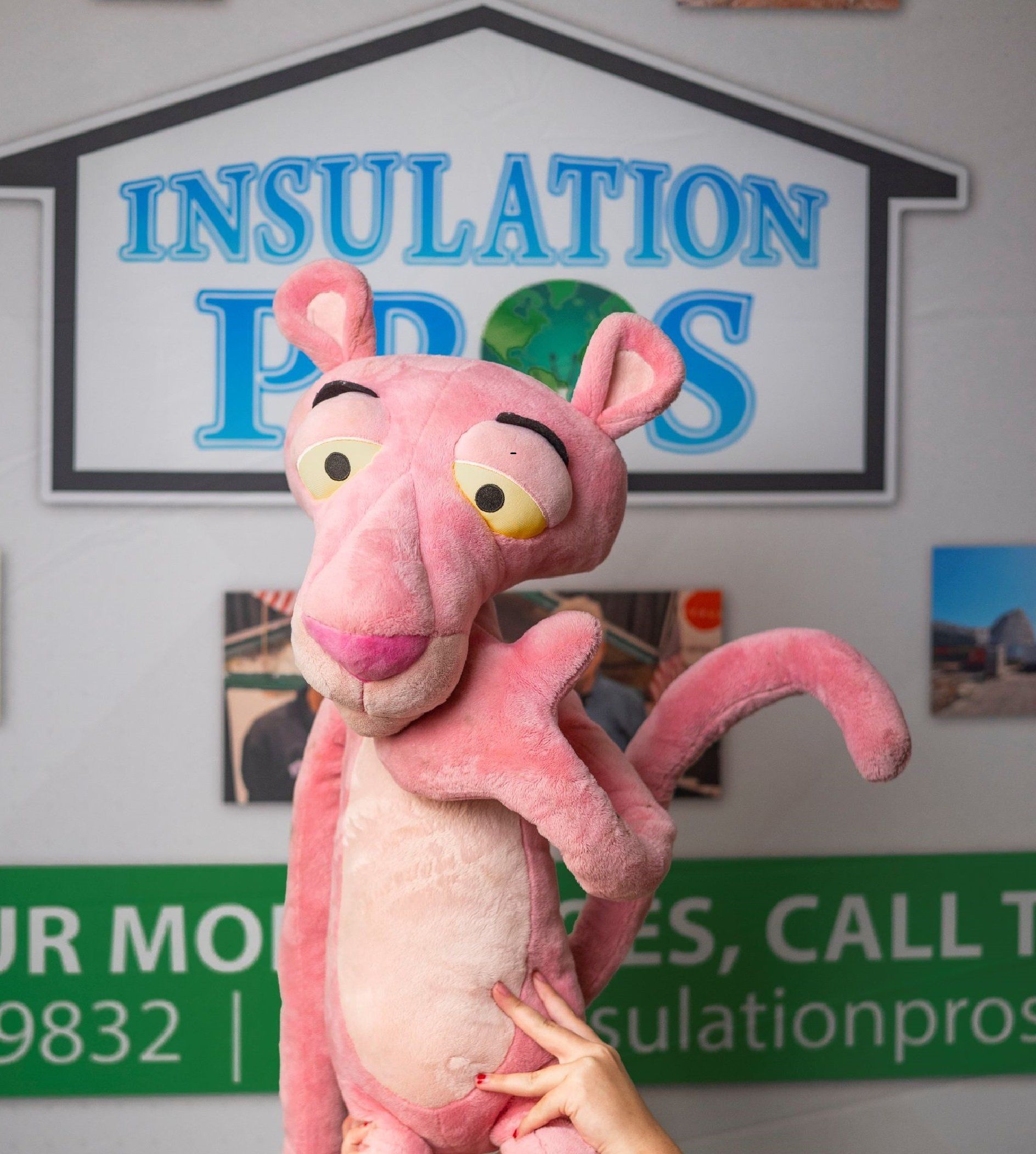 A person holding a stuffed pink panther in front of a sign that says insulation pros