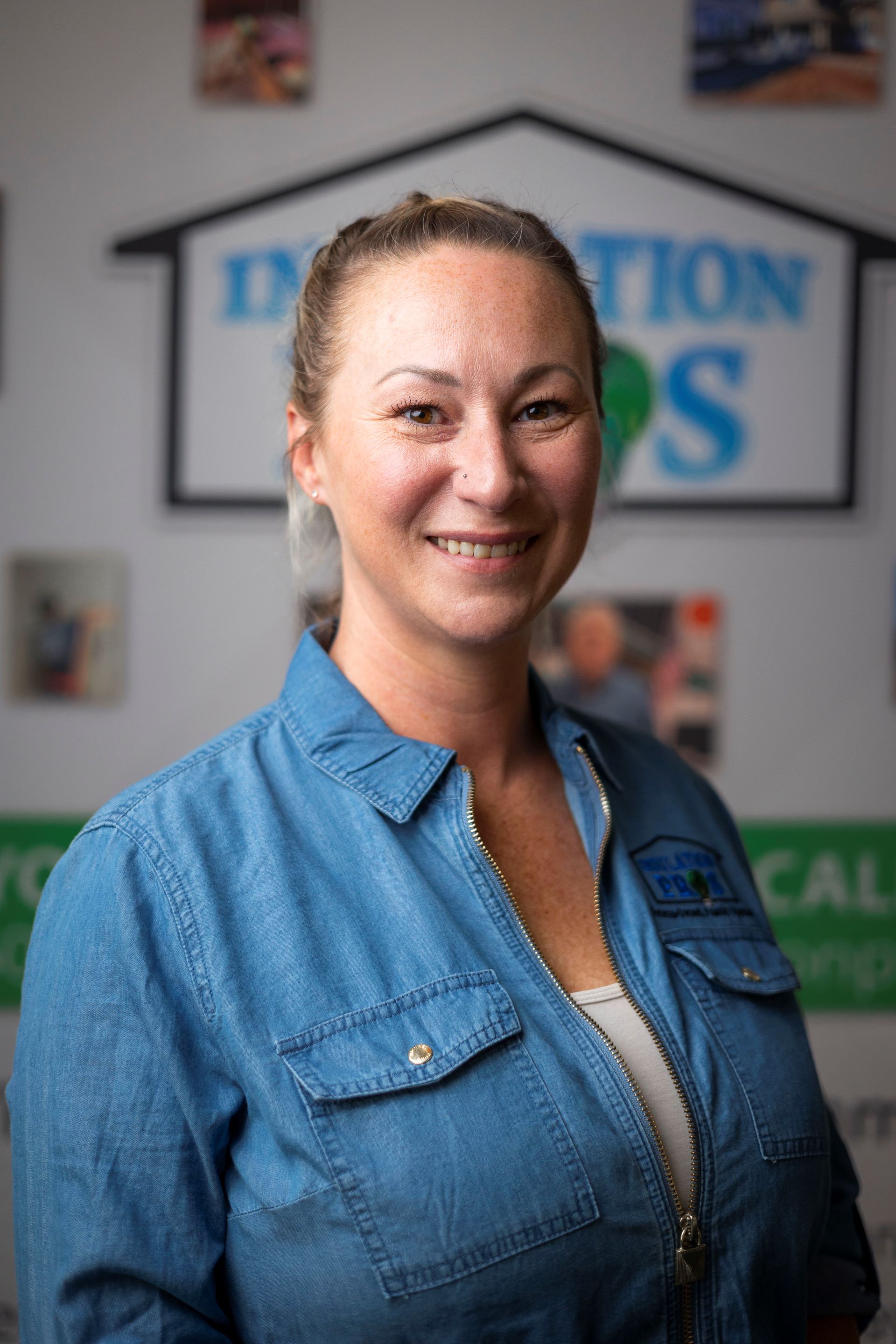 A woman in a blue denim shirt is smiling for the camera.