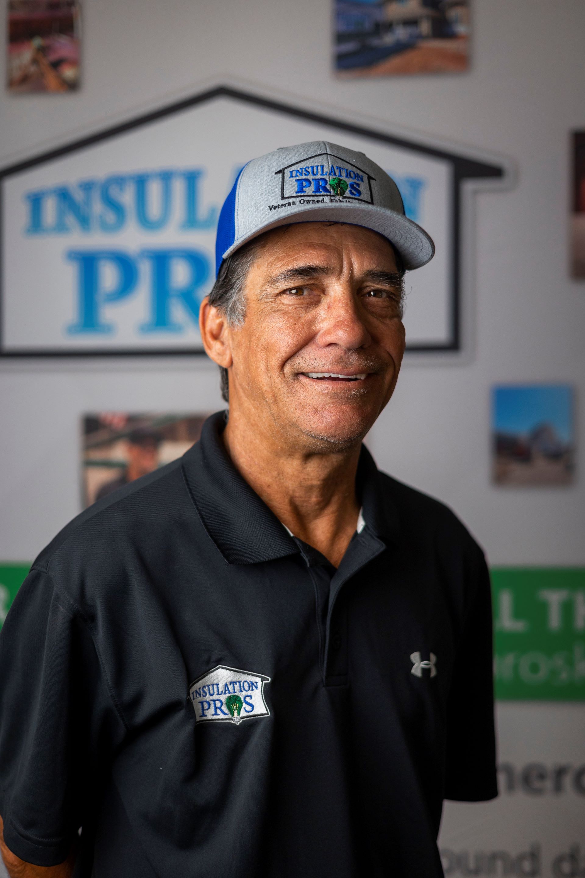 A man wearing a hat and a black shirt is standing in front of a sign that says insulation pro.
