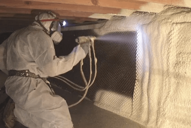 A man is spraying foam on a wall in a basement.