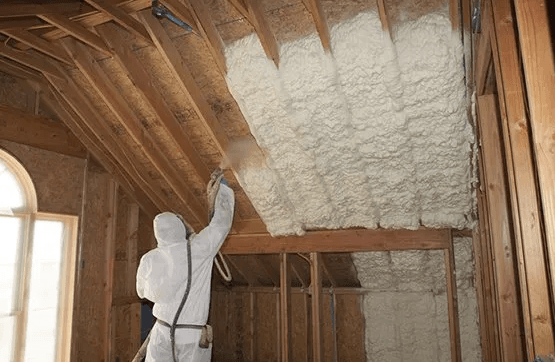 A man is spraying foam on the ceiling of a house.
