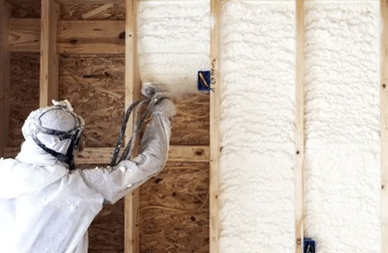 A man is spraying insulation on a wooden wall.