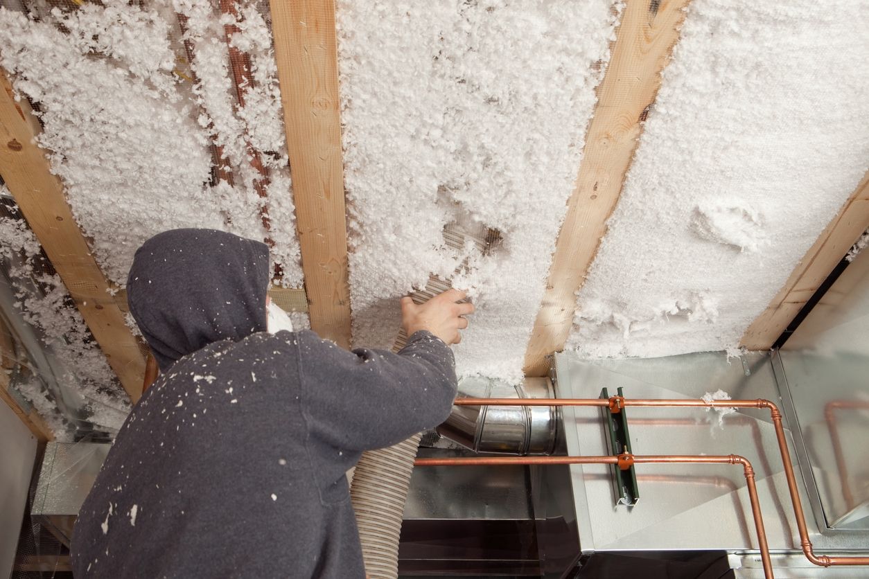A male worker installing a blown in blanket insulation between house floor joist