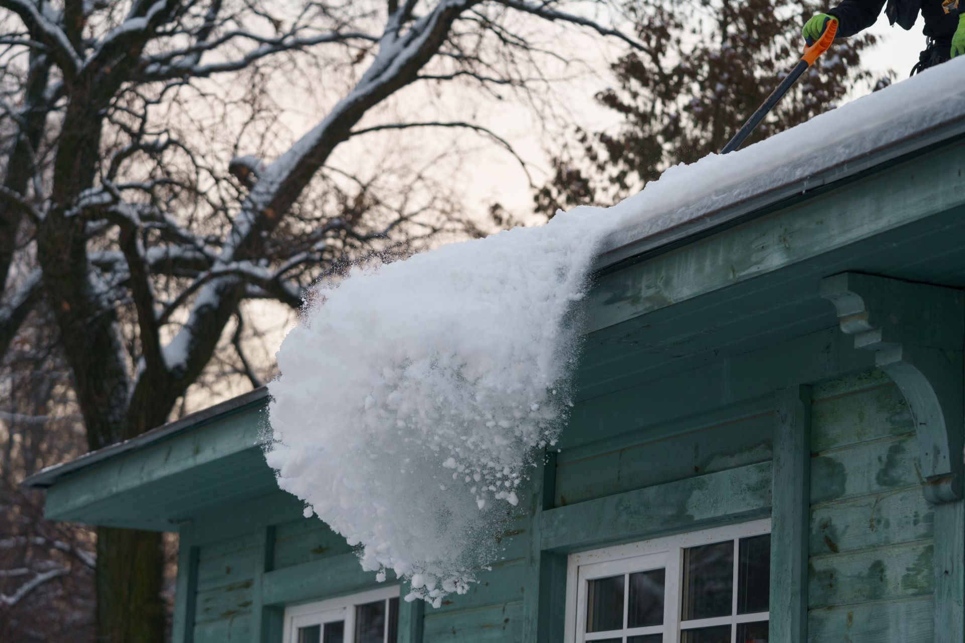 A person is shoveling snow off the roof of a house.