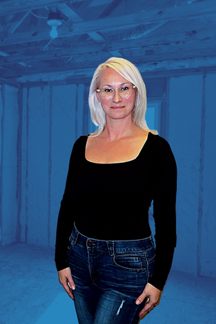 A woman wearing glasses and a black shirt is standing in front of a blue wall.