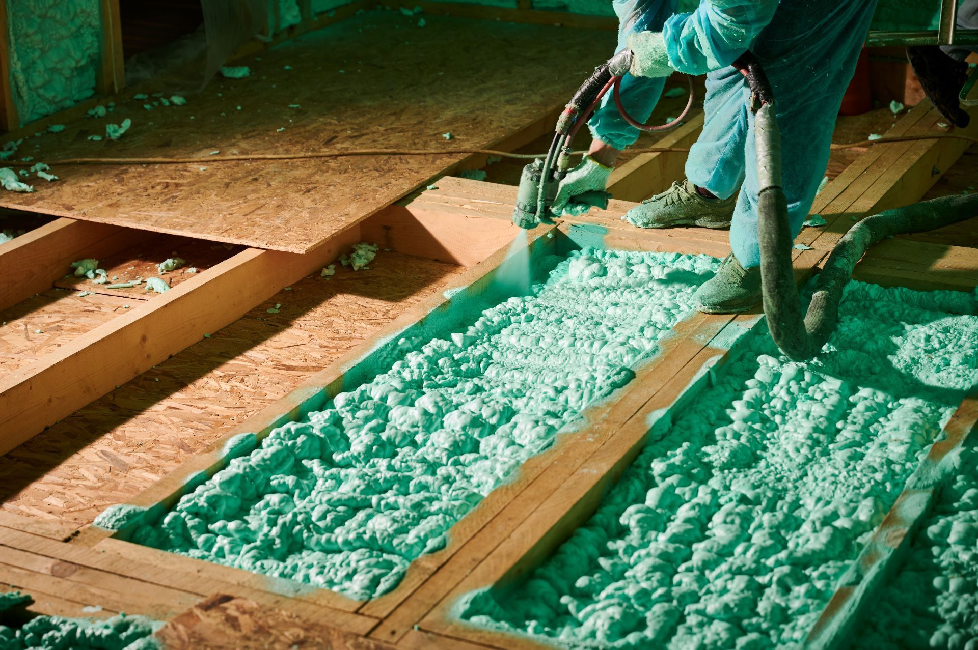 A man is spraying green insulation on a wooden floor.